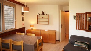 Een gezellige woonkamer met een houten eettafel, stoelen, een bank en een kleine keuken met een plank en een lamp.