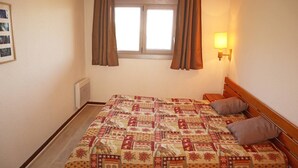 Een slaapkamer met een bed, een raam met gordijnen, een wandlamp en een radiator.