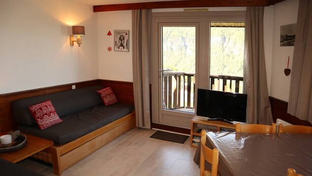 Een gezellige kamer met een bank, een televisie, een eettafel en een raam met gordijnen.
