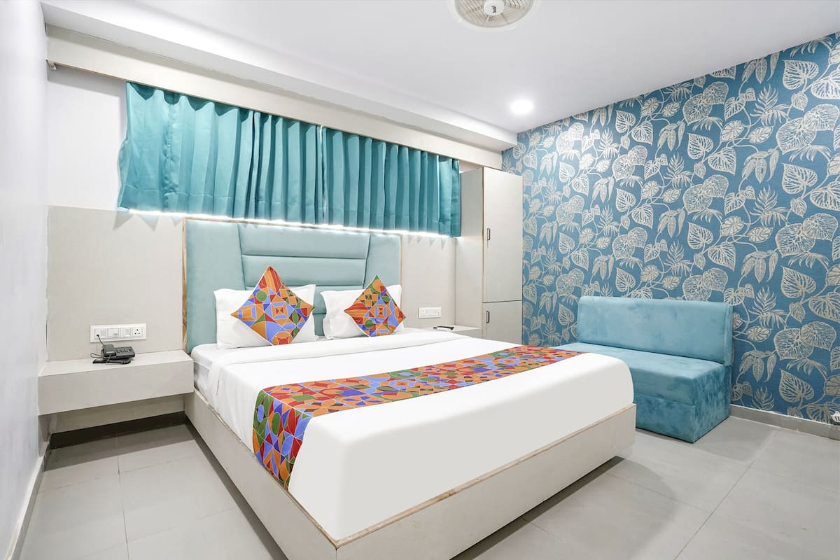 A modern bedroom with a bed, bedside tables, a nightstand, a blue sofa, and patterned wallpaper.