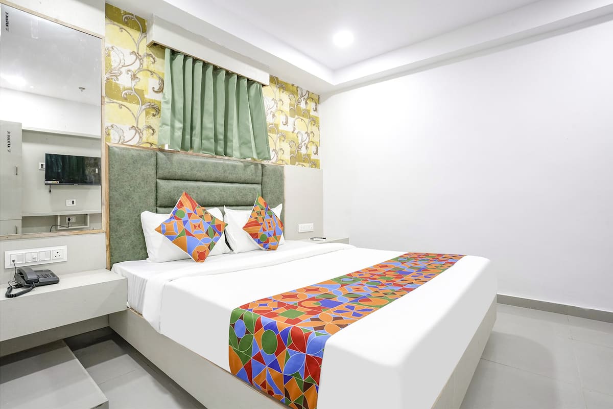 A modern hotel room with a large bed, a bedside table with a phone, a TV, and a green curtain.