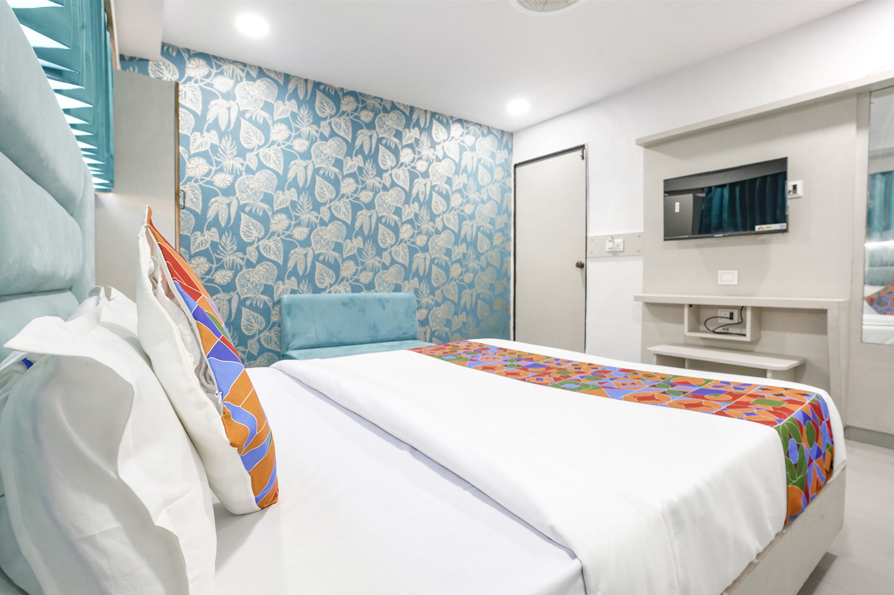 Une chambre d’hôtel avec un lit, un mur orné d’un motif bleu, un téléviseur fixé au mur et une porte.