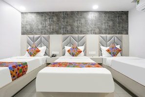A hotel room with three beds, each with a unique geometric-patterned pillow and a colorful quilt.