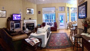 A living room with a fireplace, a television, and a dining area with chairs. - UPSCALE NE TALLAHASSEE QUIET, SECURE RESIDENCE FULLY EQUIPPED (Tallahassee)