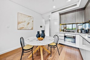 A modern kitchen with white cabinets, a marble dining table, and a large window overlooking the city.