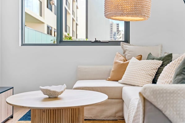 A modern living room with a sofa, a round coffee table, and a large window with a view of buildings.