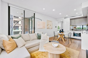 A modern living room with a sofa, a round coffee table, and a dining area with a white table and chairs.