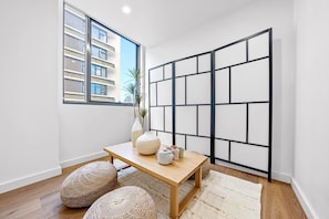 A modern room with a wooden table, two poufs, a vase, and a black partition.