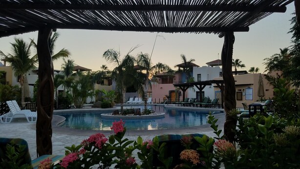 Ein Poolbereich eines Resorts mit Liegestühlen, einer kleinen Wasserattraktion und Palmen.