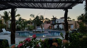 Zwembadgedeelte van een resort met ligbedden, een kleine waterattractie en palmbomen.