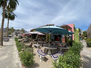 An outdoor patio area with stone tables and benches, surrounded by greenery and palm trees.