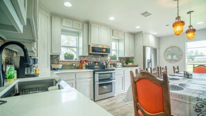 A modern kitchen with white cabinetry, a stainless steel refrigerator, an oven, and a microwave. There is a dining table with chairs and a chandelier above. - ❤️ Pickleball, Pool Table, Ping Pong, 4Bd 2bath quiet edition on quiet lake cove. (Granbury)
