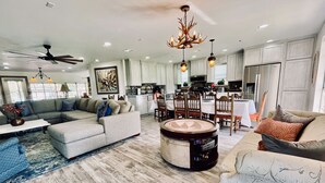 A spacious living room with a sectional sofa, a round coffee table, and a dining area with wooden chairs and a chandelier. - ❤️ Pickleball, Pool Table, Ping Pong, 4Bd 2bath quiet edition on quiet lake cove. (Granbury)
