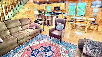 A spacious living area with a large rug, sofas, a coffee table, and a staircase leading to an upper level.