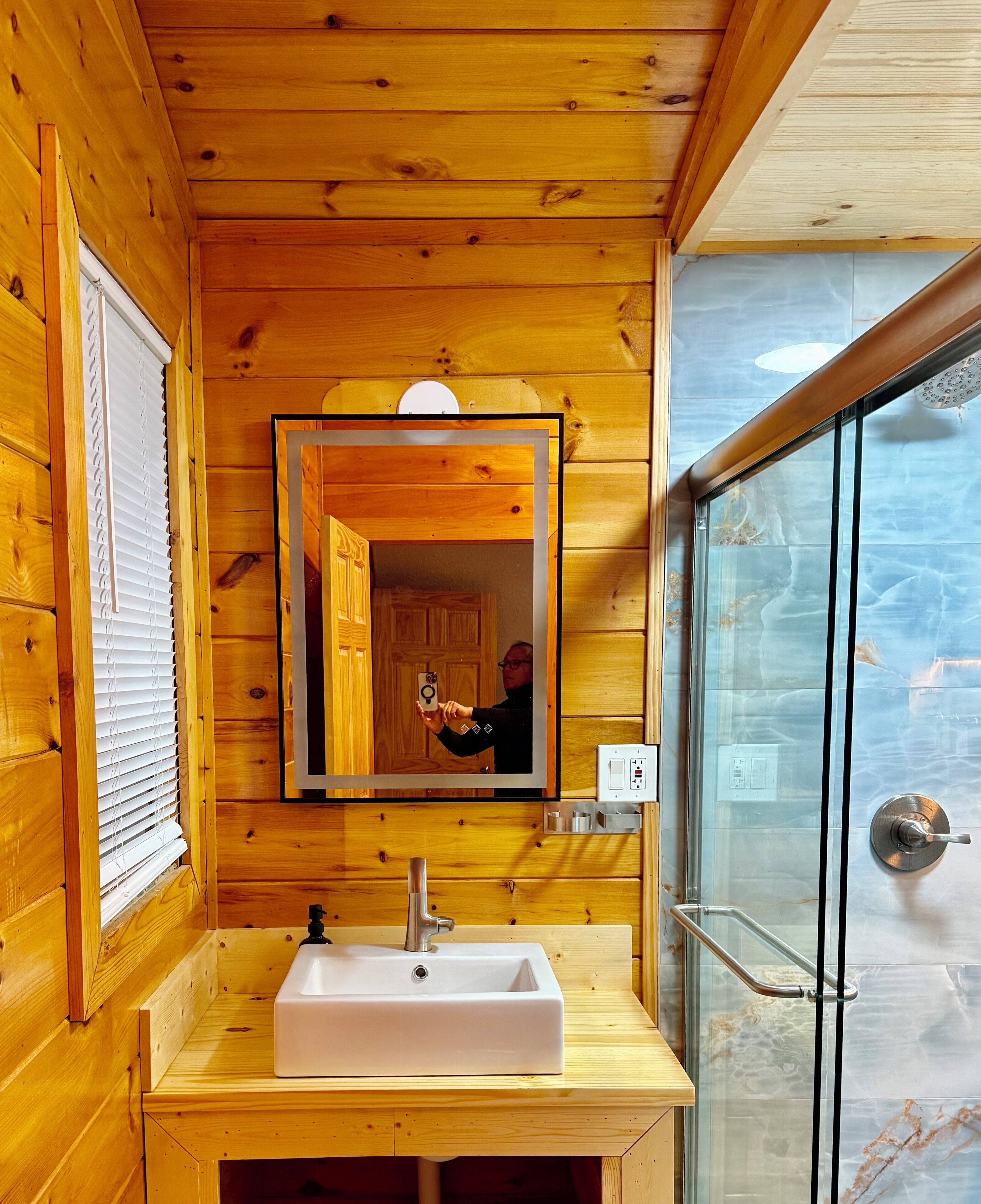 A wooden cabin bathroom with a wooden vanity, a mirror, and a glass shower enclosure.