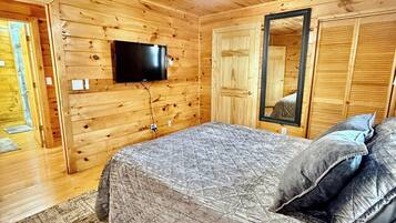 A wooden-paneled bedroom with a bed, a flat-screen TV mounted on the wall, and a large mirror.