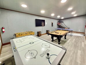 Een kamer met een tafelvoetbaltafel, een poolbiljart en een pingpongtafel.