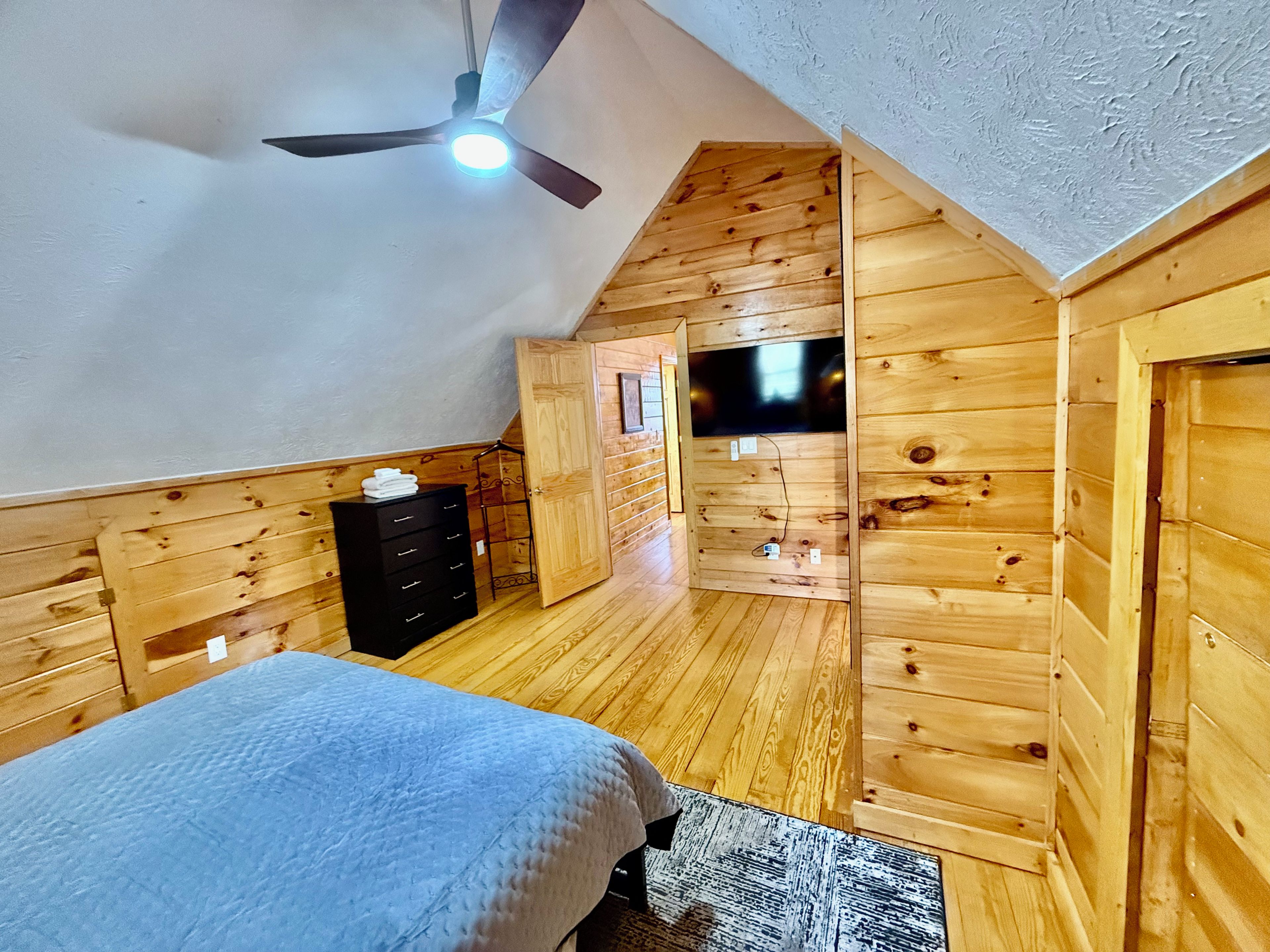 Una camera da letto con un letto, una cassettiera, pareti in legno, una ventola a soffitto e un televisore.