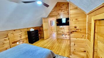 Una camera da letto con un letto, una cassettiera, pareti in legno, una ventola a soffitto e un televisore.