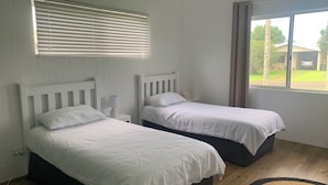 A room with two beds, a window with curtains, and a view of the outside.