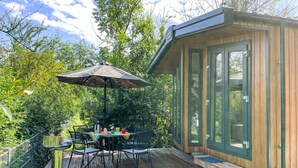 Une terrasse en bois avec une table et des chaises, un parasol et un petit bâtiment doté de grandes fenêtres.