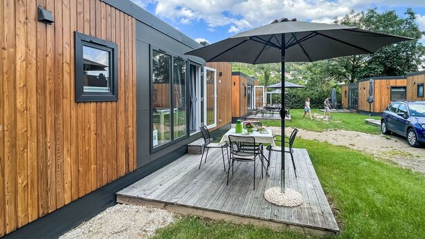 A modern outdoor patio with a wooden deck, a table with chairs, and a large umbrella.