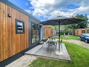 A modern outdoor patio with a wooden deck, a table with chairs, and a large umbrella. - Tiny Haus Elena by Interhome (Riedenburg)