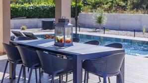 A poolside dining area with a table and chairs, a lantern, and umbrellas. - Villa Shea by Interhome (Labin)