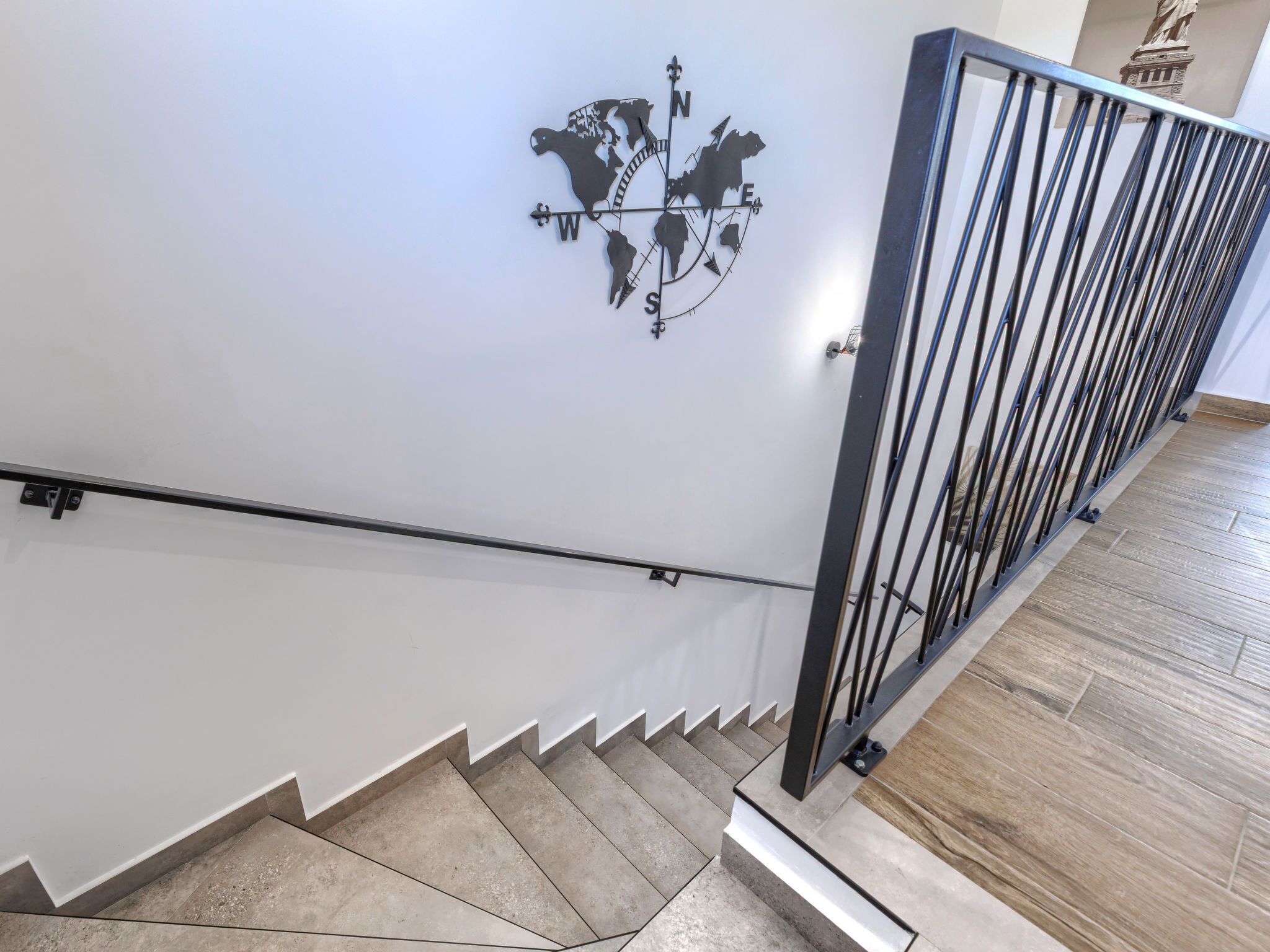 A staircase with a metal railing and a compass wall art.