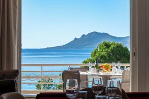 A dining area with a table set for two, overlooking a scenic view of the sea and a mountain. - RARE! Luxury apartment on the Croisette (Cannes)