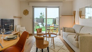 Een moderne woonkamer met een bank, een eettafel met stoelen, een televisie en een groot raam met uitzicht op het landschap.