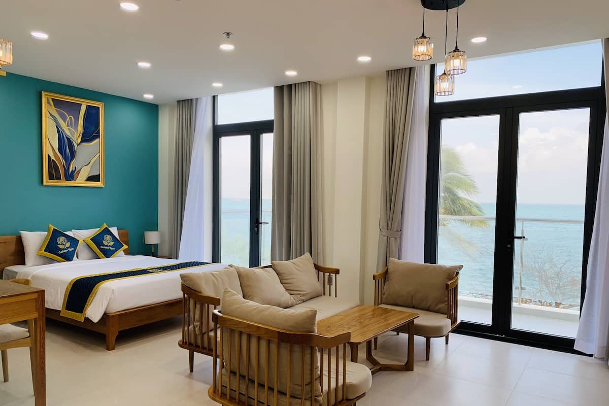 A hotel room with a bed, a sofa, a table, and a view of the sea.