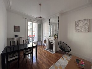 A dining area with a wooden table and chairs, a fireplace, and a view of the outside balcony. - Appartement au Cœur de Paris (Paris)