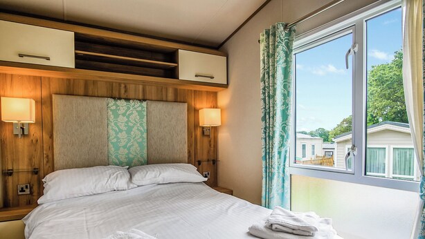 Une chambre d’hôtel avec un lit, deux lampes de chevet, une fenêtre avec des rideaux et une vue sur d’autres immeubles.