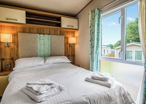 Ein Hotelzimmer mit Bett, zwei Nachttischlampen, einem Fenster mit Vorhängen und Blick auf andere Gebäude.