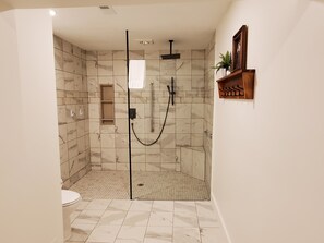 A bathroom with a shower, toilet, and marble tiles.