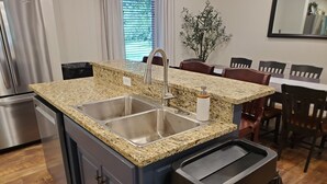 A kitchen with granite countertops, stainless steel sink, and a trash can.
