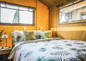 Ein Bett mit Bettwäsche mit Blattmuster, eine Nachttischlampe und ein Fenster mit Vorhängen.