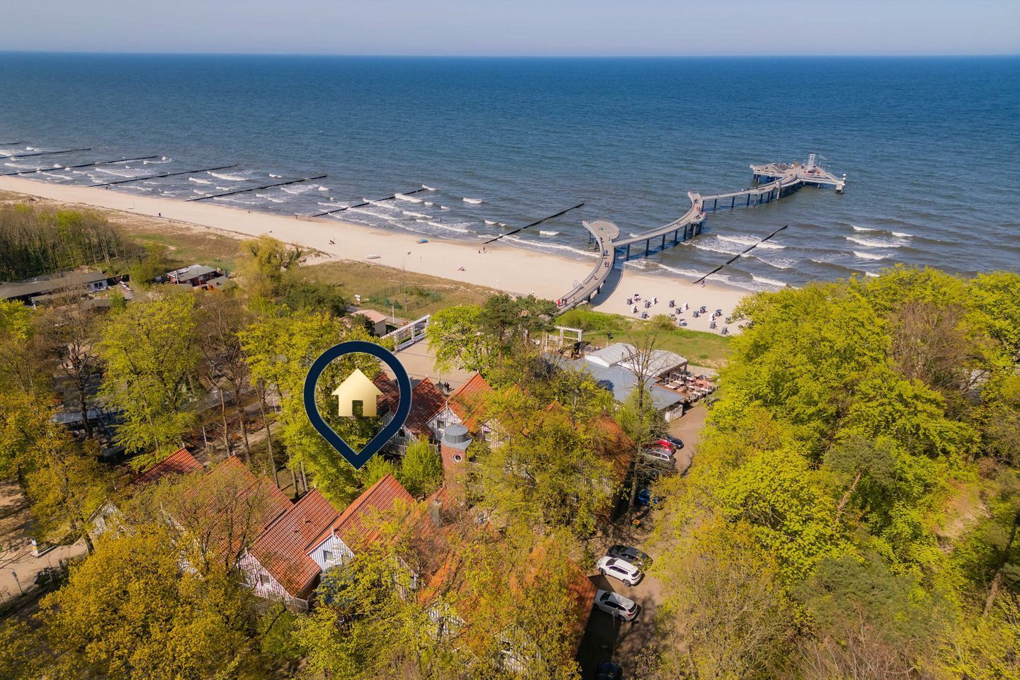 Eine Küstenlandschaft mit einem Steg, einem Strand und einer markierten Stelle eines von Bäumen umgebenen Gebäudes.