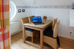 En spiseplads med et træbord, fletstole, en bærbar computer og en vase med blomster.
