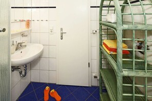 Un baño con un lavamanos blanco, piso de azulejos azules y una estantería metálica verde.