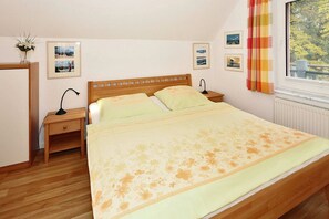 A bedroom with a wooden bed, a nightstand, a desk, and a window with curtains.
