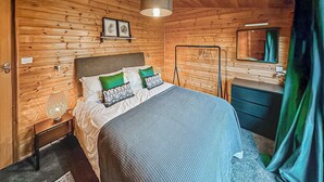A wooden-paneled room with a bed, bedside table, lamp, and a mirror. - Stylish two bedroom lodge, perfect for couples or families. (Cowbridge)
