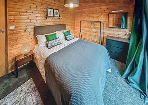 Ein Zimmer mit Holzwänden, einem Bett, einem Nachttisch, einer Lampe und einem Spiegel.