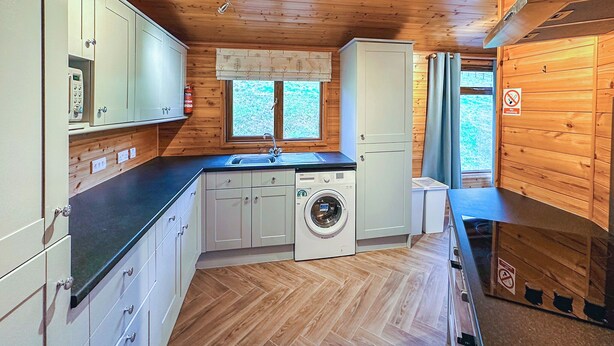 A compact kitchen with wooden walls, a washing machine, and a sink. - Stylish two bedroom lodge, perfect for couples or families. (Cowbridge)