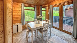 A wooden interior with a dining table, chairs, and large windows. - Stylish two bedroom lodge, perfect for couples or families. (Cowbridge)