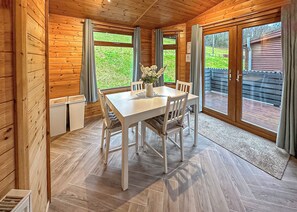A wooden interior with a dining table, chairs, and large windows.