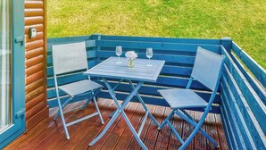 A blue deck with a table and chairs, a glass door, and a grassy field in the background. - Stylish two bedroom lodge, perfect for couples or families. (Cowbridge)