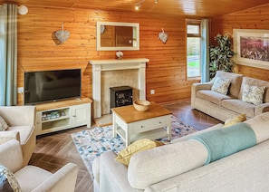 A cozy living room with a TV, fireplace, sofa, and wooden walls.
