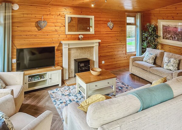 Ein gemütliches Wohnzimmer mit Fernseher, Kamin, Sofa und Holzwänden.